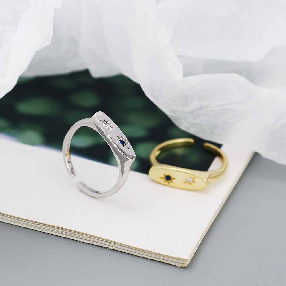 Minimalist silver and gold open bands with star-set gemstones, modern jewellery on paper background.