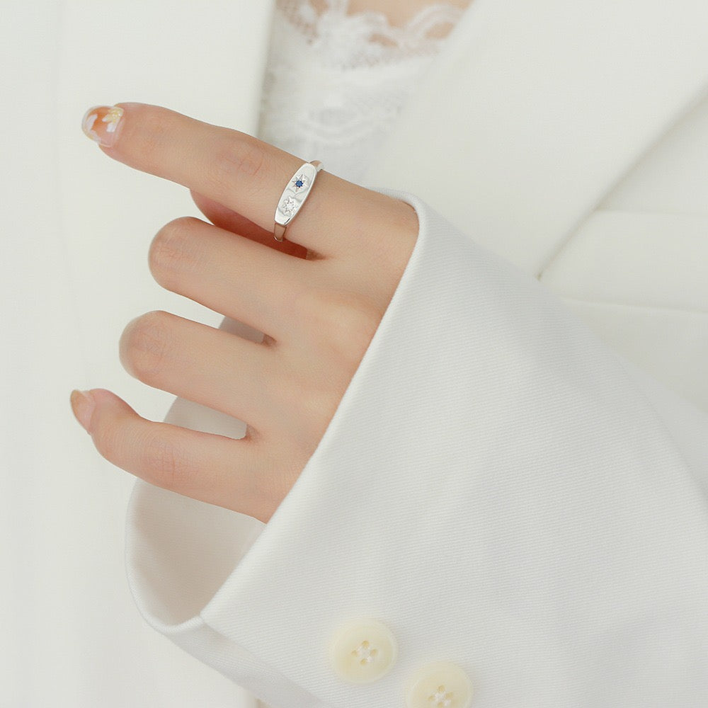 Minimalist silver ring with blue gemstone worn on hand in white blazer sleeve