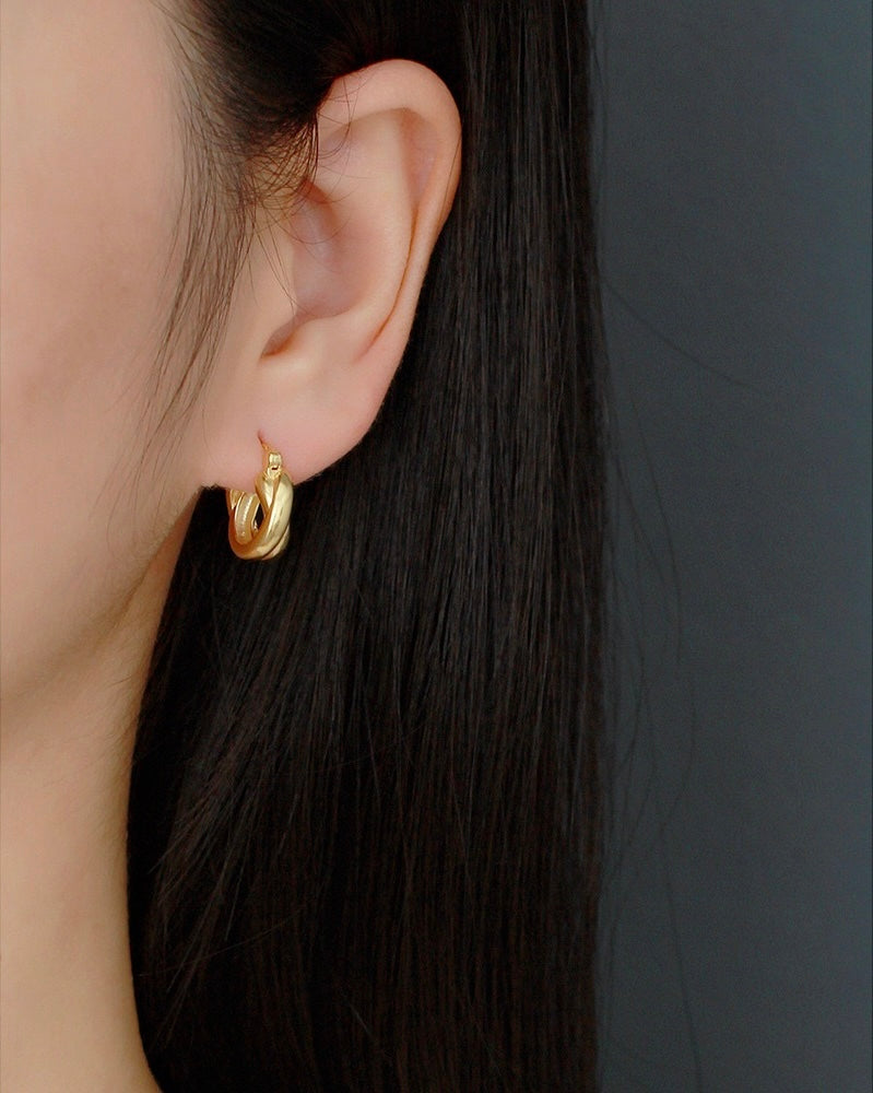 Minimalist gold twisted hoop earring worn on ear, modern precious metal jewelry close-up