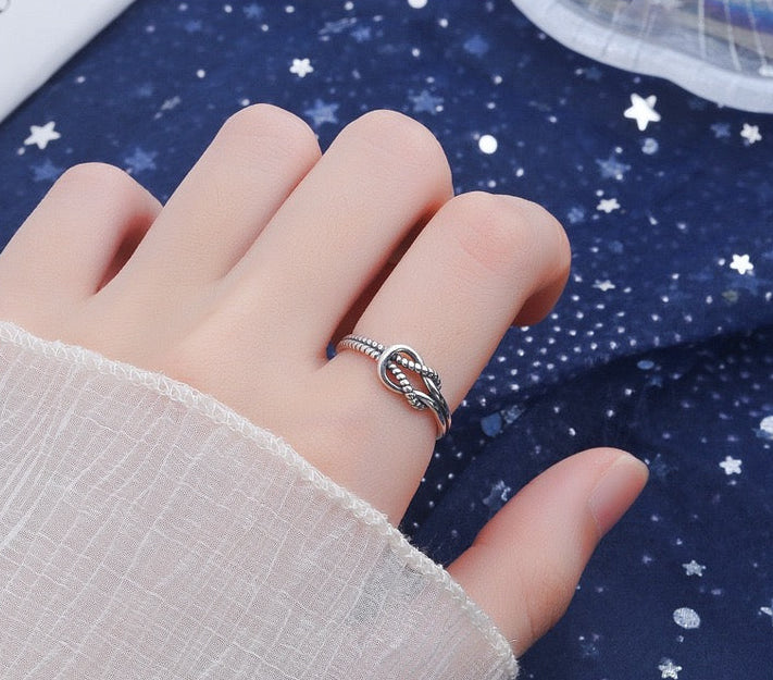 Hand wearing a minimalist silver knot ring with beaded detail on a star-patterned background
