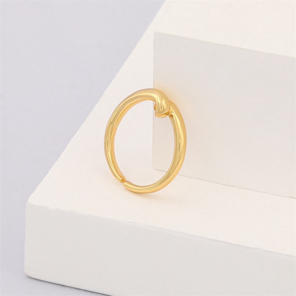 Minimalist gold hoop earring with knot detail on white geometric display