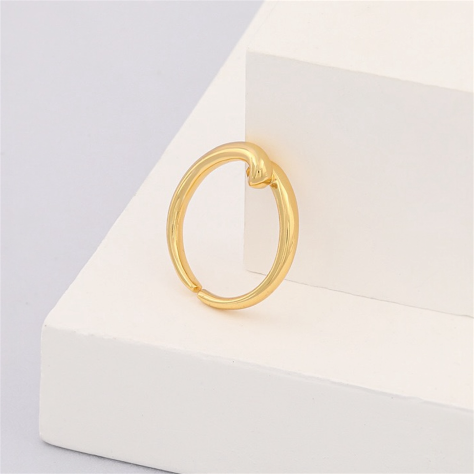 Minimalist gold hoop earring with knot detail on white geometric display
