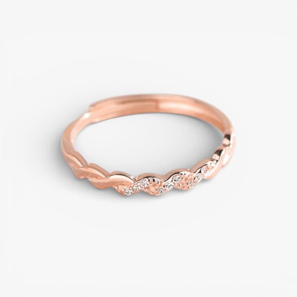 Rose gold minimalist twisted band ring with delicate embedded stones on white background