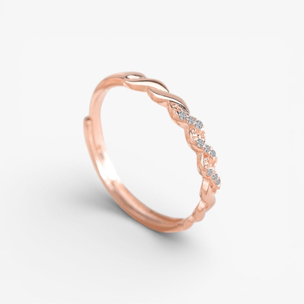 Rose gold twisted band ring with embedded small clear stones on a white background