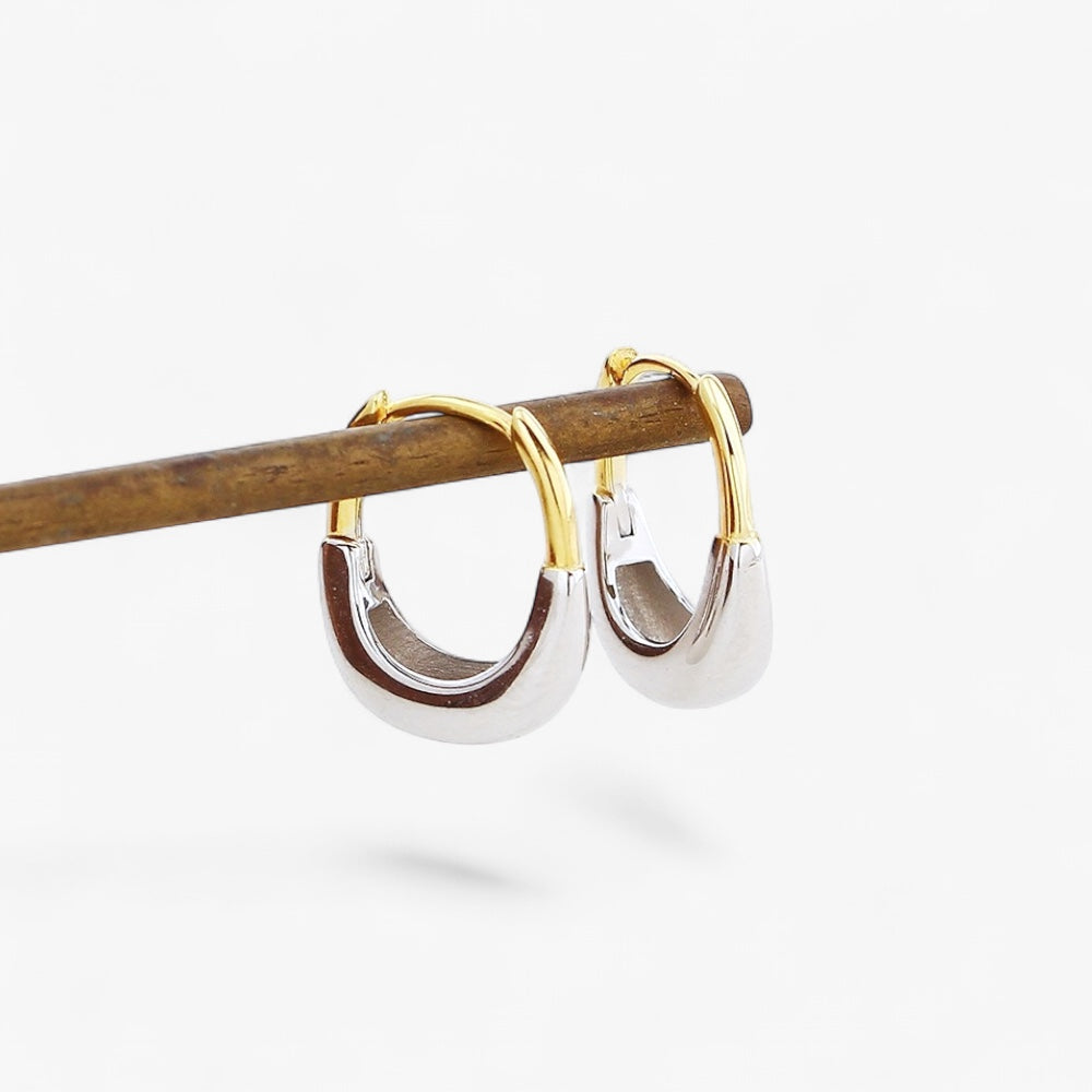 Minimalist two-tone gold and silver hoop earrings on a wooden rod, modern jewelry