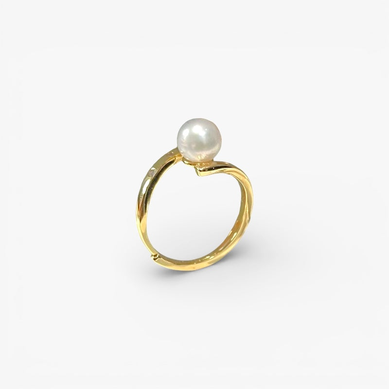 Minimalist gold ring with a single round white pearl on a plain background