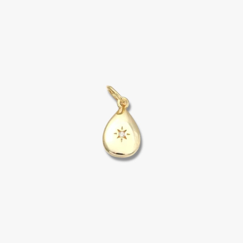 Gold teardrop pendant with engraved star design and small central gemstone on white background