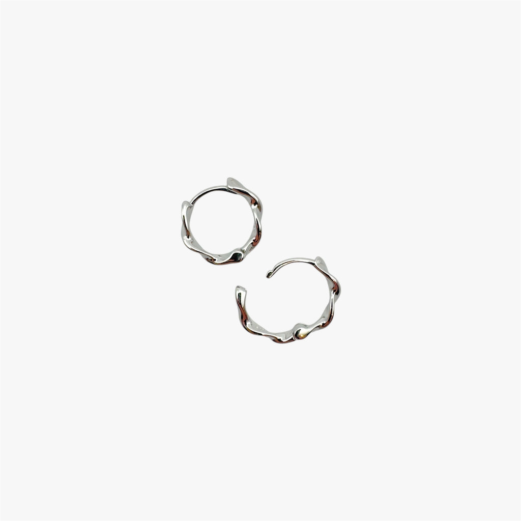 Pair of organically-shaped silver huggie hoop earrings at an above view.