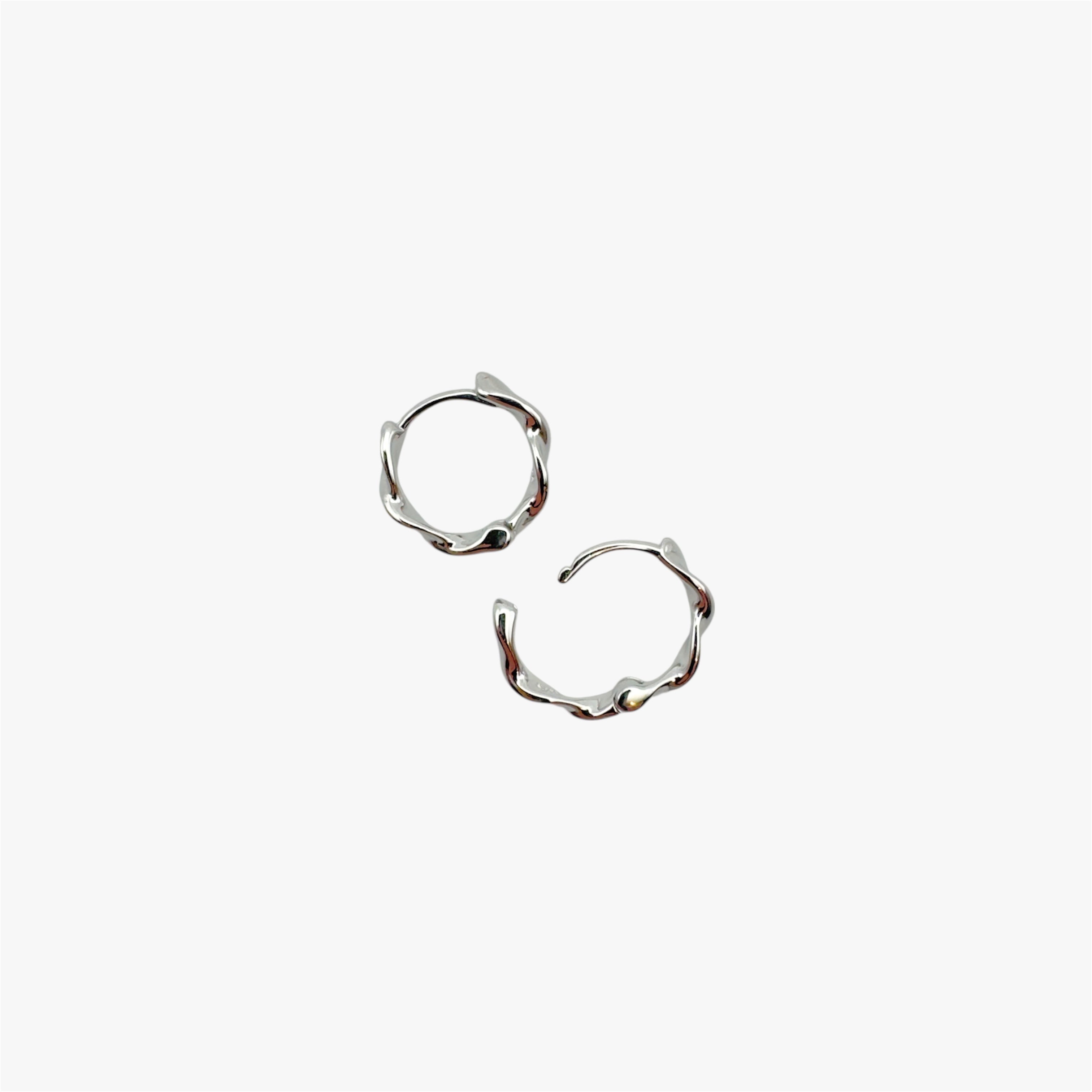 Pair of organically-shaped silver huggie hoop earrings at an above view.